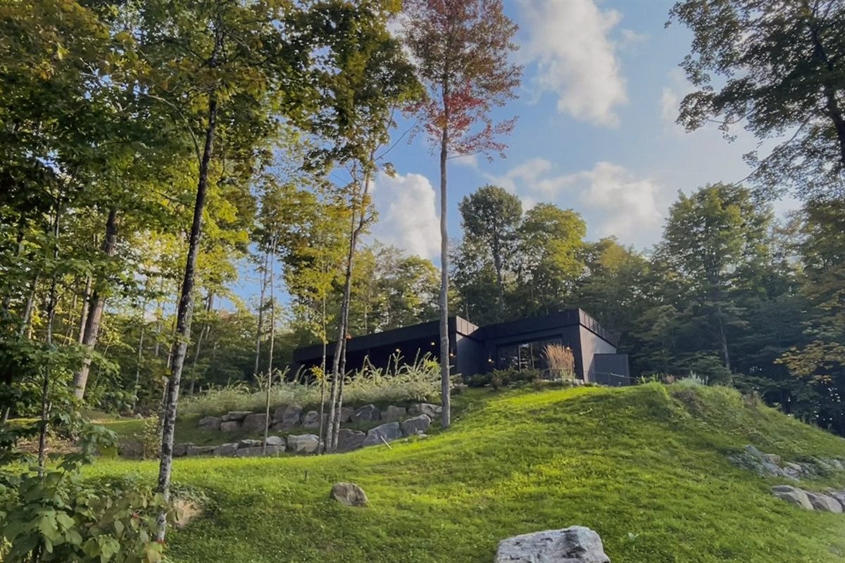 La maison longue et basse le long de sa colline verte, vue d’en bas