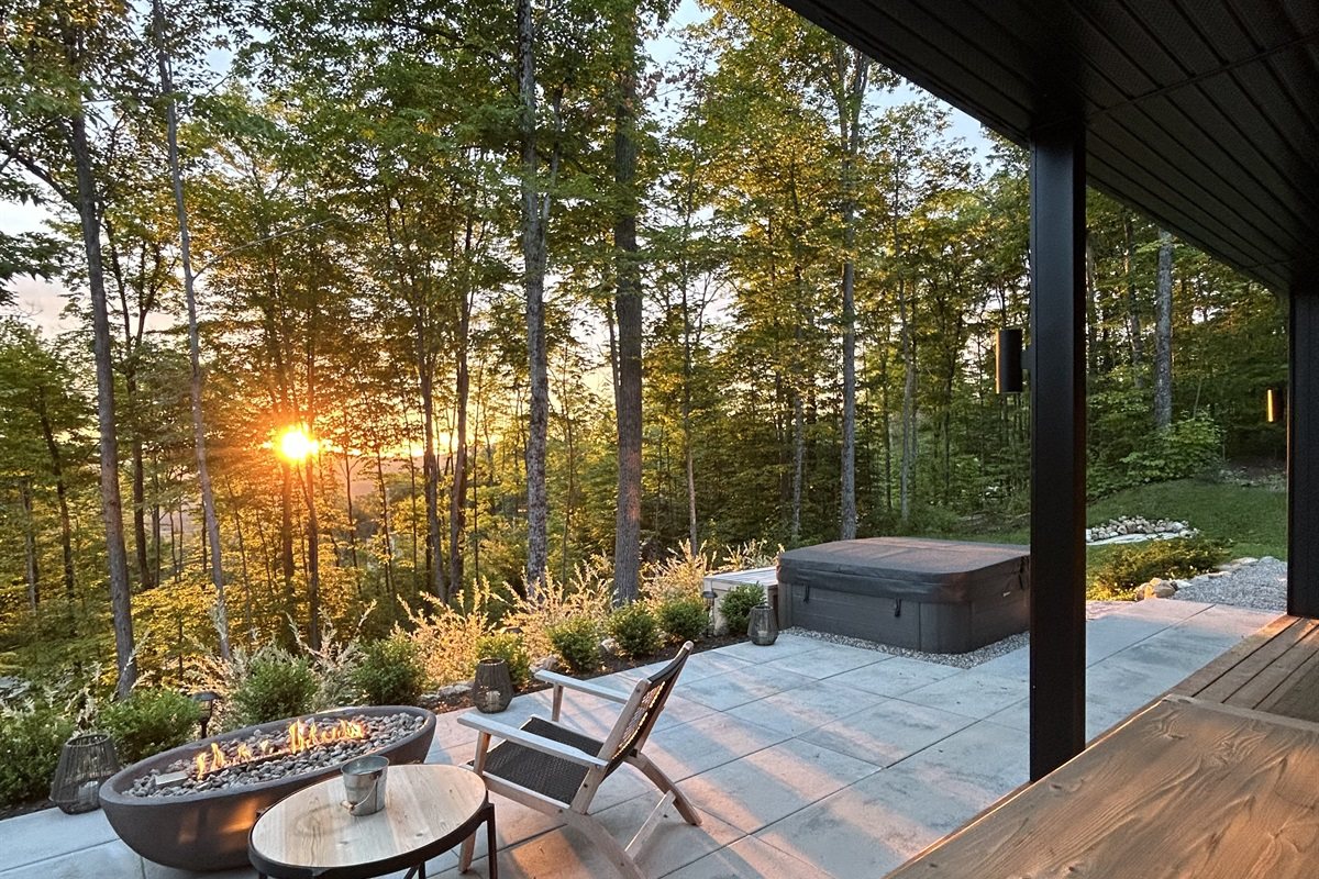 La terrasse couverte au coucher du soleil, le foyer allumé et le spa au fond
